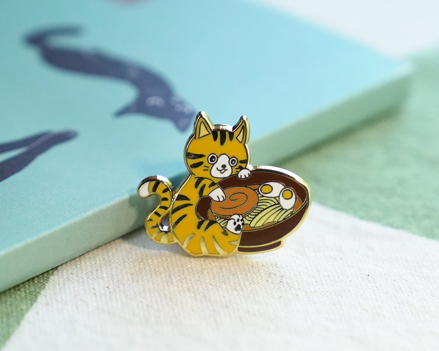 Cat-shaped enamel pin on a textured surface with a light blue background