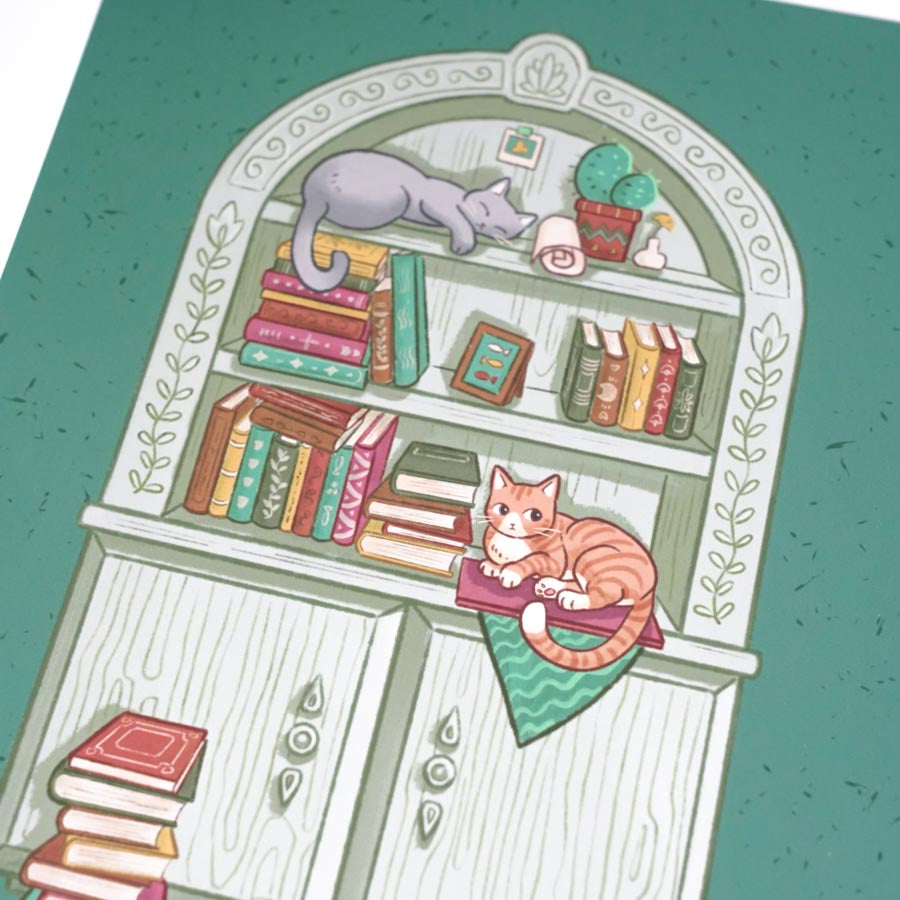 close up on a print of a cute gray bookcase filled with books and trinkets with 2 cats lying on it. Background is green.