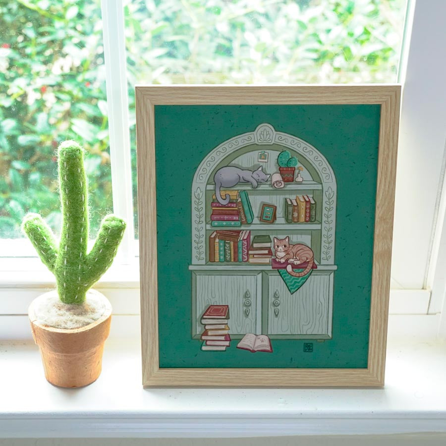 A print of a cute gray bookcase filled with books and trinkets with 2 cats lying on it by the window. Background is green.