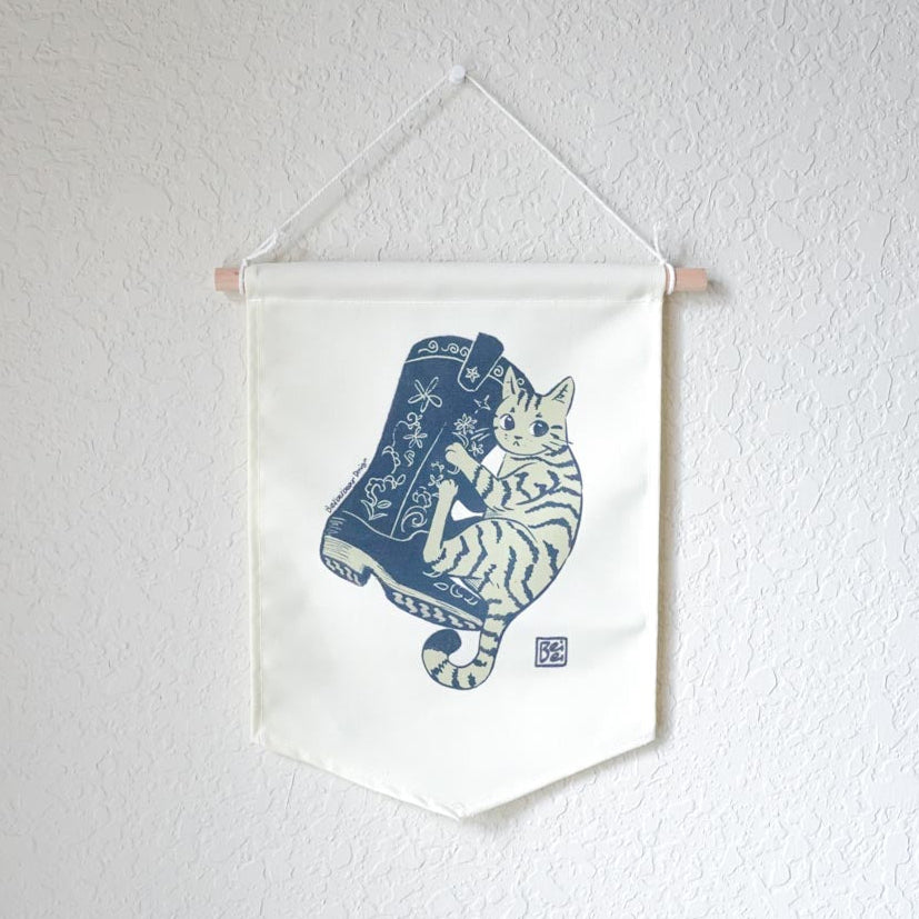 A canvas banner featuring simple illustration of a stripped cat hugging a floral cowboy boot