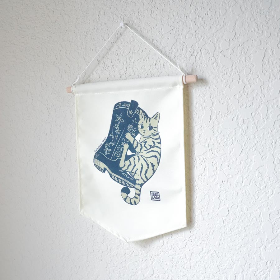 A canvas banner featuring simple illustration of a stripped cat hugging a floral cowboy boot