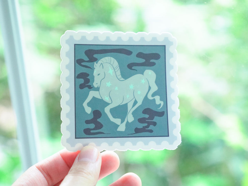 Sticker with a horse design held by a hand against a blurred green background