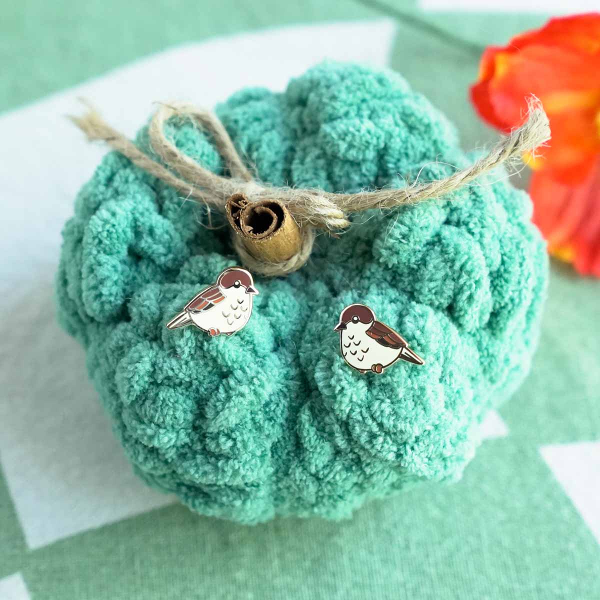Bird-shaped earrings on a textured teal ball with twine