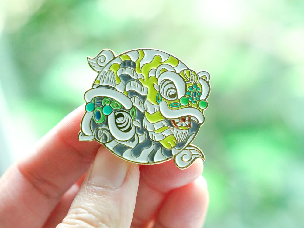 Decorative Chinese lion pin held by a hand with a blurred green background