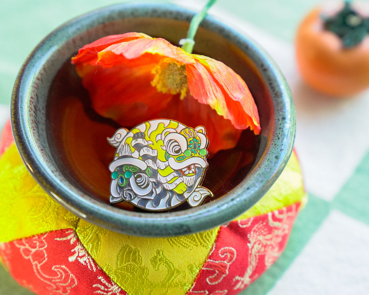 Tea cup with a decorative lion pin and a red flower, on a colorful fabric background.